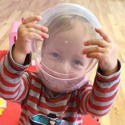 Kita-Kind schaut durch druchsichtigen Behälter